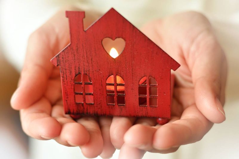 hands holding red house with candle 